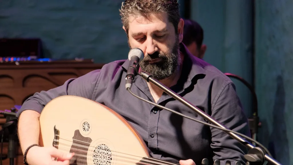 Musician playing laouto and singing into a microphone.