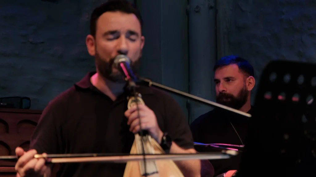 Musician playing lyra and singing with eyes closed.