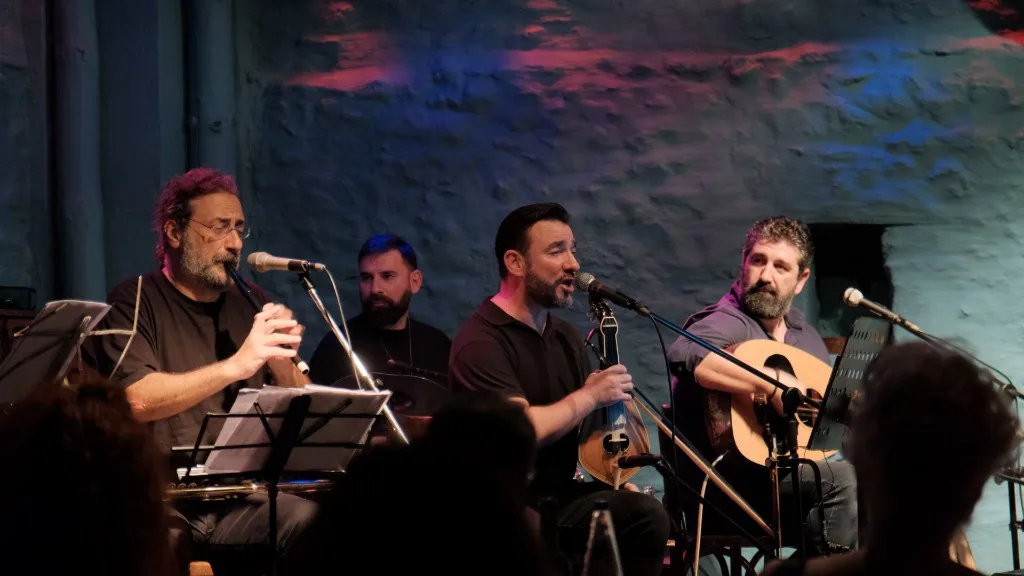 Four musicians on stage under colored lighting.
