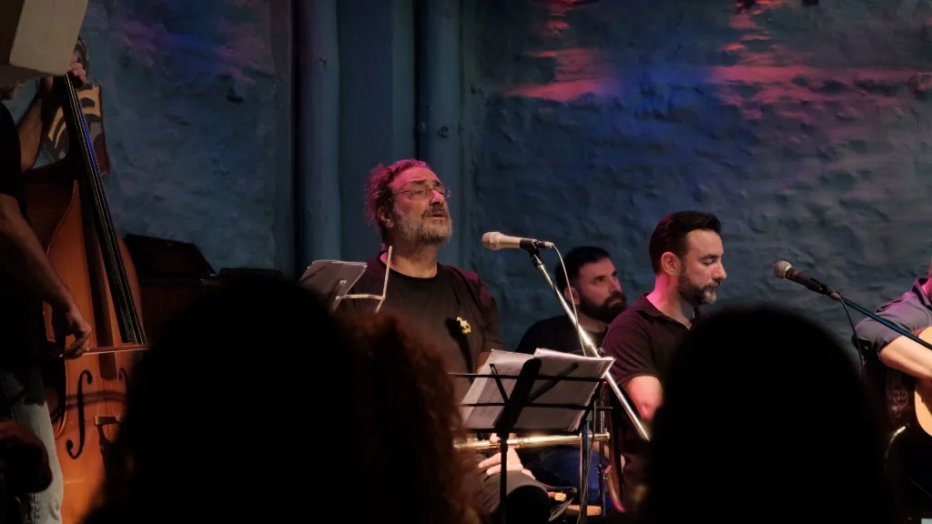 Musician singing at the microphone with a flute, facing the audience.