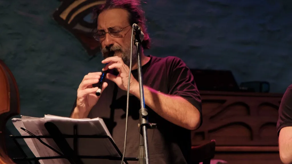Musician playing a wooden flute on stage beside a music stand.
