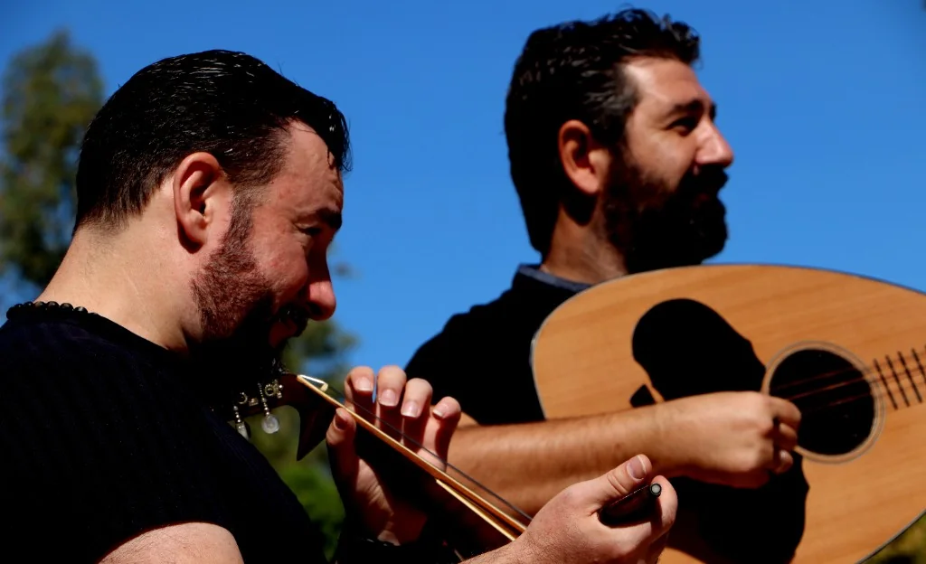 Musicians playing lyra and laouto under open sky.